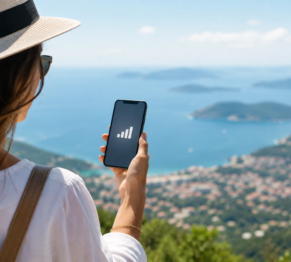 Traveller in a straw hat holding her iPhone above a bay dotted with islands, full signal on screen